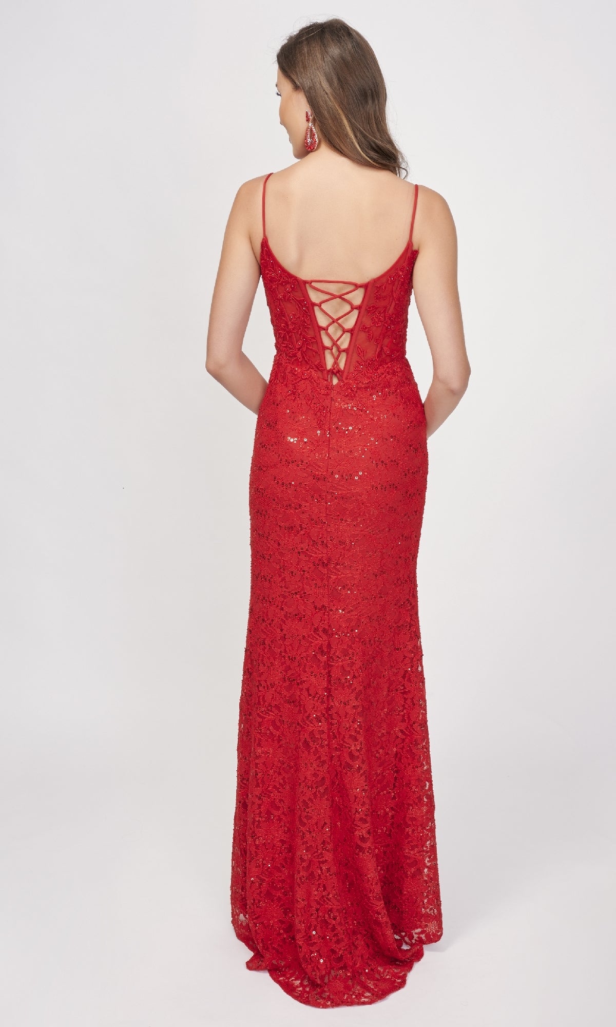 A woman models the Nina Canacci 1568 long formal dress, featuring sleeveless sequin lace, a lace-up back, and a thigh-high slit, standing against a plain white background.
